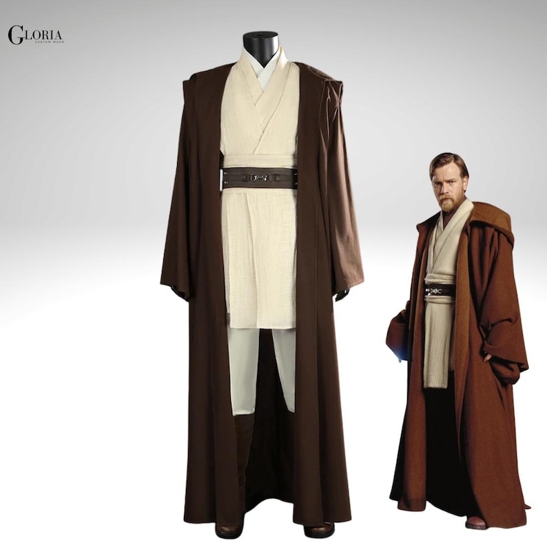 Pu&ograve; includere: Un set di costumi composto da una lunga tunica marrone con cappuccio, una tunica color crema con scollo a incrocio, una maglia interna abbinata, una cintura marrone scuro con fibbia centrale e pantaloni color crema. Il testo GLORIA &egrave; visibile in alto a sinistra.