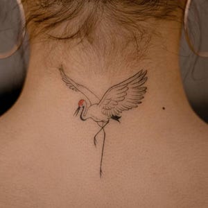 Könnte beinhalten: Schwarzes und rotes Kranich-Tattoo auf dem Nacken. Der Kranich ist mit ausgebreiteten Flügeln, einem roten Kopf und einem langen, dünnen Bein dargestellt. Das Tattoo ist ein zartes, minimalistisches Design.
