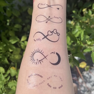 Può includere: Un set di cinque tatuaggi temporanei neri con disegni del simbolo dell'infinito. I design includono nomi come David, Susan, Lucas e Ashley, cuori, un motivo sole e luna con la lettera J e il testo and forever has no end.
