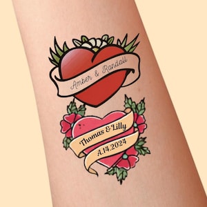 May include: Two temporary tattoos featuring red hearts with green leaves. The top heart has a banner with the text Amber & Randall. The bottom heart has a banner with the text Thomas & Lilly and A.14.2024. Both designs use bold black outlines.