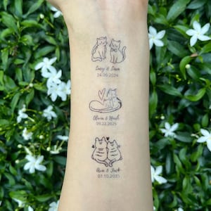 May include: Three temporary tattoos on skin featuring black line art of cat pairs. The first shows two cats with the text Lucy & Liam 24.06.2024. The second shows two cats with a heart and text Olivia & Noah 09.22.2025. The third shows two cats with text Ava & Jack 07.10.2025.