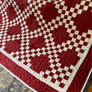 May include: A red and white checkered quilt with a quilted pattern of small circles. The quilt is folded in half and the edges are trimmed with white fabric.