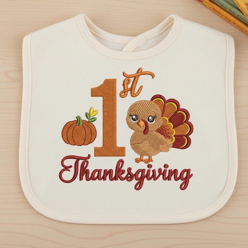 May include: An off-white baby bib featuring an embroidered design with a large orange number 1, the text 1st Thanksgiving in dark red, a small orange pumpkin with green leaves, and a brown turkey with a red and yellow tail.