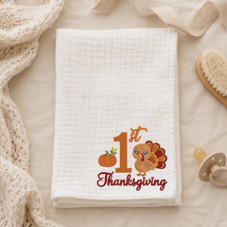 May include: A white muslin swaddle blanket featuring an embroidered design with a large orange number 1, a small orange pumpkin, a cartoon turkey with brown and red feathers, and the red text 1st Thanksgiving printed below the graphic.