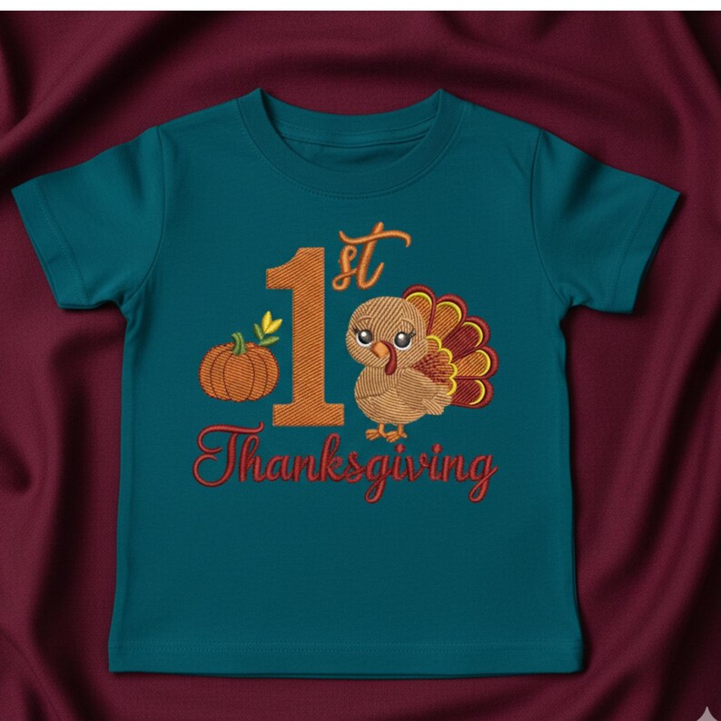 May include: A teal short-sleeved t-shirt featuring an embroidered design with the text 1st Thanksgiving. The graphic includes a large orange number one, a small orange pumpkin with green leaves, and a brown turkey with colorful tail feathers.