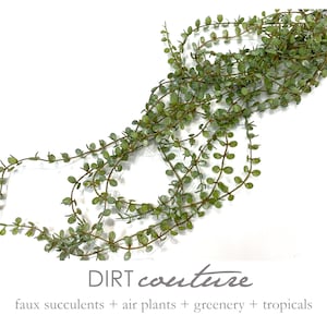 May include: A long strand of faux greenery with small, round, green leaves. The greenery is arranged in a loose, flowing pattern. The text "DIRT couture" is visible at the bottom of the image, along with the tagline "faux succulents + air plants + greenery + tropicals".
