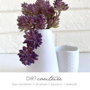 May include: A white ceramic vase holds faux purple succulents. The vase is next to a small white cup with a dotted texture. The image includes the text "DIRT couture" and "faux succulents + air plants + greenery + tropicals".