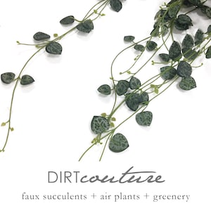 May include: A long strand of faux green leafy vines with white speckles. The vines are hanging down against a white background. The text "DIRTcouture" and "faux succulents + air plants + greenery" is at the bottom of the image.