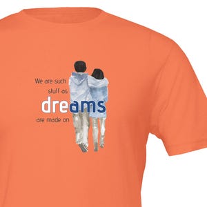Könnte beinhalten: Orangefarbenes T-Shirt mit einer Aquarellillustration von zwei Personen, die gehen, mit dem Wort "dreams" in Blau. Der Text "We are such stuff as dreams are made on" ist ebenfalls auf dem T-Shirt aufgedruckt.