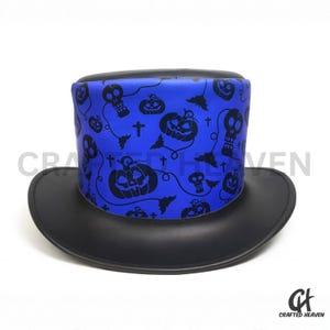 Puede incluir: Un sombrero de copa negro con una banda azul con un patrón de Halloween de calaveras, calabazas, murciélagos y cruces. El sombrero tiene un ala ancha y una corona cilíndrica, perfecto para un disfraz.