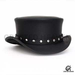 Puede incluir: Un sombrero de copa de cuero negro con ala ancha y una banda de tachuelas plateadas. El sombrero tiene una copa cilíndrica y un ala ligeramente curvada. Un estilo clásico, adecuado para ocasiones formales.