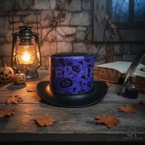 Puede incluir: Un sombrero de copa negro con una banda morada con motivos de Halloween, como calabazas, murciélagos y cruces. El sombrero está sobre una mesa de madera con hojas de otoño, una linterna y calabazas en el fondo.