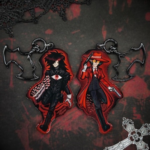 May include: Two anime-style keyrings featuring characters in black and red outfits. One keyring shows a character with a large eye and a creature-like arm. The other keyring depicts a character in a red coat holding two guns.