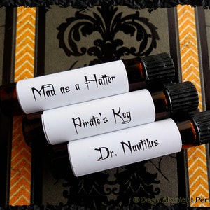 Op de afbeelding: Vier kleine glazen flesjes met zwarte dopjes en witte etiketten. De etiketten hebben de volgende tekst: "Mad as a Hatter", "Pirate's Keg", "Dr. Nautilus".