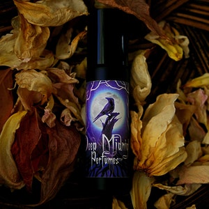 May include: A small, black roll-on bottle of perfume with a purple label featuring a raven perched on a branch under a full moon. The label reads "Deep Midnight Perfumes".