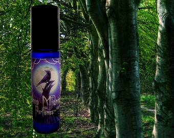 May include: A blue glass roller bottle with a label that says "Deep Midnight Perfumes" and features a black raven perched on a branch under a full moon. The bottle is in front of a background of green trees.