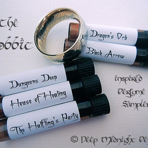 May include: A set of six small glass bottles with black caps and white labels. The labels have handwritten text that reads "Dungeons Deep", "House of Healing", "The Halfling's Party", "Dragon's Orb", "Black Arrow", and "inspired perfume sampler". The bottles are arranged in a semi-circle around a gold ring with an inscription. The text at the bottom of the image reads "© Deep Midnight Perfumes".