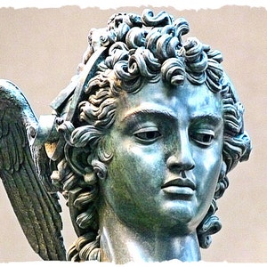 May include: Close-up of a bronze sculpture of an angel's head with curly hair and a wing.