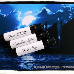 Może przedstawiać: Trzy małe szklane butelki z czarnymi korkami i białymi etykietami. Etykiety są oznaczone jako "Pieces of Eight", "Gunpowder Gertie" i "Pirate's Key". Butelki znajdują się przed niebieskim i czarnym obrazem statku płynącego po oceanie w nocy.