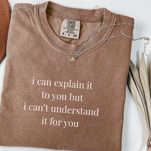 Puede incluir: Una camiseta de manga corta color espresso con cuello redondo y el texto impreso en blanco: i can explain it to you but i can't understand it for you. La camiseta presenta una etiqueta de la marca Comfort Colors en el cuello interior.