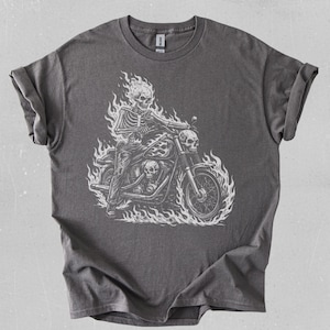 May include: Dark gray t-shirt featuring a white graphic of a skeleton riding a motorcycle engulfed in flames. The design includes a flaming skull and detailed motorcycle elements, creating a bold, edgy aesthetic.