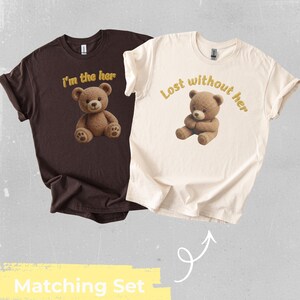 Puede incluir: Dos camisetas, una marrón y otra crema, se muestran juntas. La camiseta marrón tiene el texto "I'm the her" y un gráfico de oso de peluche. La camiseta crema dice "Lost without her" con un oso a juego. Las palabras "Matching Set" están en la parte inferior.