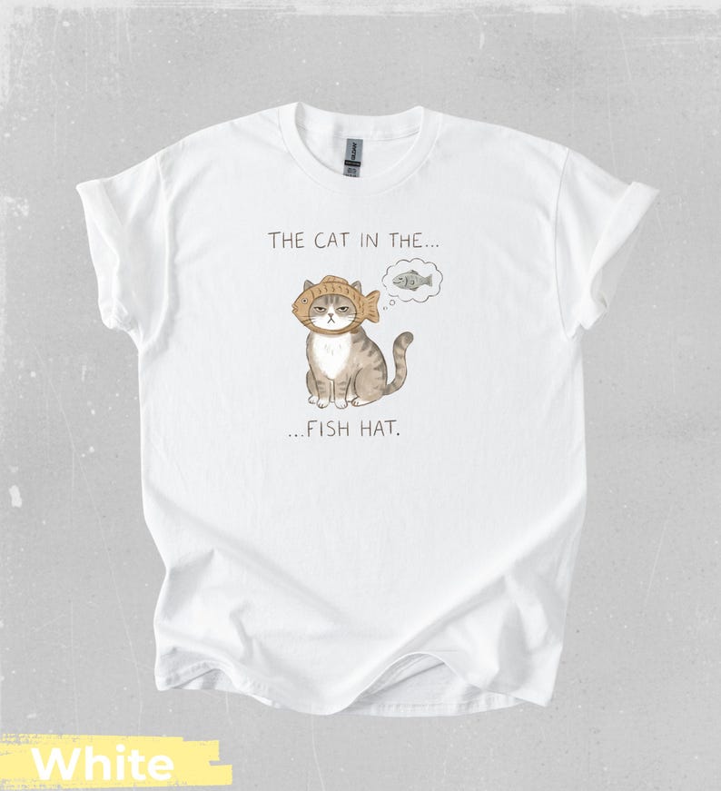 May include: White t-shirt featuring a whimsical illustration of a cat wearing a fish hat, with a thought bubble showing a fish. The text on the shirt reads "THE CAT IN THE... FISH HAT."