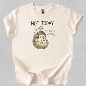 Puede incluir: Camiseta color crema con el texto "NOT TODAY." y un erizo de dibujos animados con auriculares, con una nube de tormenta encima. Un bocadillo dice "Nope don't even ask."