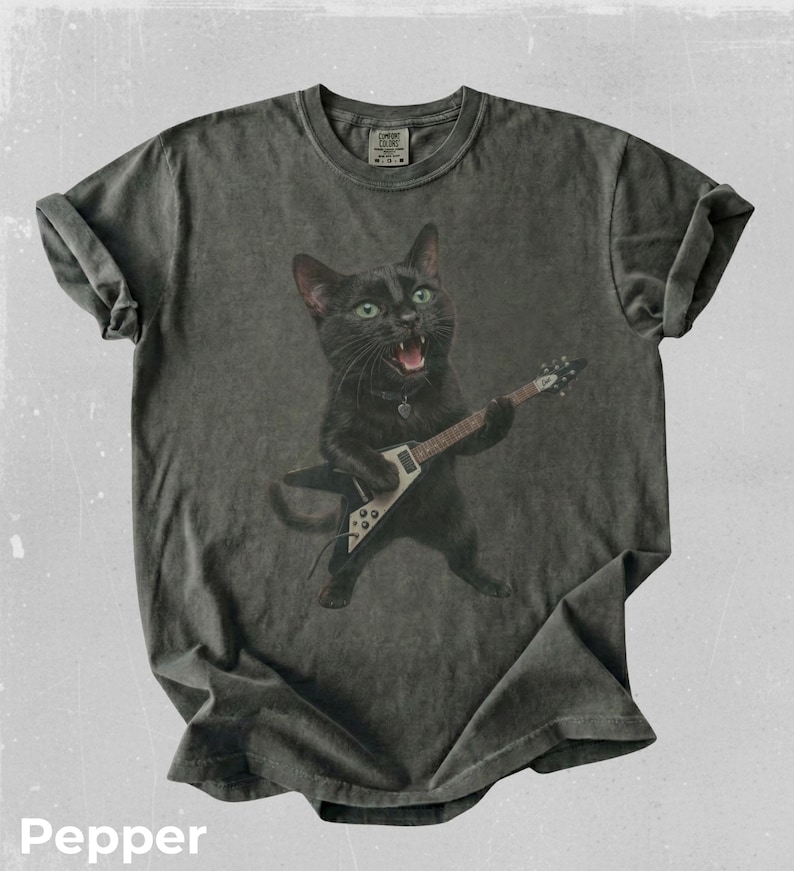 Peut inclure: Un t-shirt gris anthracite &agrave; manches courtes orn&eacute; d'un motif repr&eacute;sentant un chat noir aux yeux verts jouant d'une guitare &eacute;lectrique blanche et noire. Le chat a la gueule ouverte comme s'il chantait. Le t-shirt a un col rond et un aspect d&eacute;lav&eacute;.