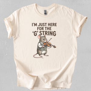 Puede incluir: Camiseta color crema con el texto "I'M JUST HERE FOR THE 'G' STRING". Un ratón de dibujos animados con chaleco toca el violín. La camiseta es de un material suave.