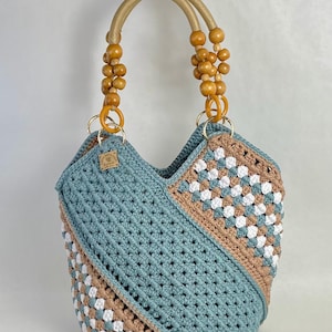 Könnte beinhalten: Eine gehäkelte Tragetasche mit einem geometrischen Muster in Blau und Braun. Die Tasche hat Griffe aus Holzperlen.