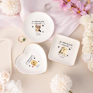 Könnte beinhalten: Drei weiße Keramik-Ringschalen mit goldenen Rändern. Eine ist rund, eine herzförmig und eine quadratisch. Jede Schale zeigt eine Haustierillustration und den Text "My Humans Are Getting Married" oder "Our Humans Are Getting Married" mit einem Datum.