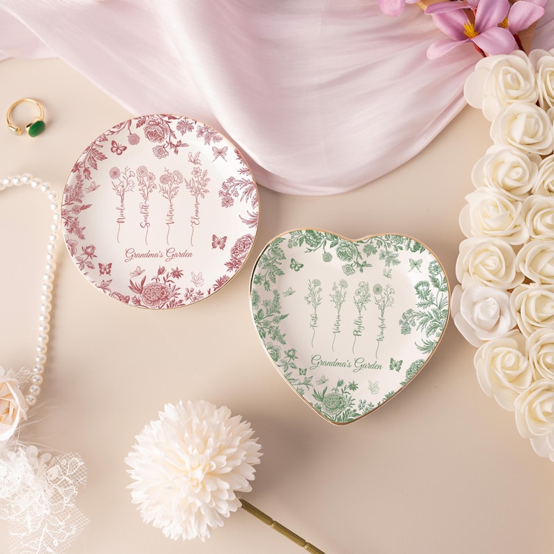 Pu&ograve; includere: Due piatti decorativi con disegni floreali. Uno &egrave; rotondo con un motivo floreale rosso e bianco, l'altro a forma di cuore con un motivo floreale verde e bianco. Entrambi i piatti hanno bordi dorati e il testo "Grandma's Garden".