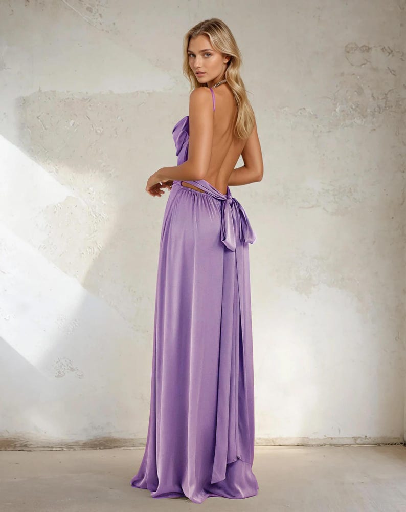 K&ouml;nnte beinhalten: Ein langes, flie&szlig;endes lavendelfarbenes Kleid mit tiefem R&uuml;ckenausschnitt und Schleife in der Taille. Das Kleid hat d&uuml;nne Spaghettitr&auml;ger und ein drapiertes Oberteil. Das Model blickt in die Kamera, der R&uuml;cken ist teilweise frei.
