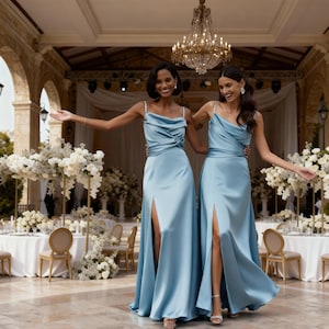 K&ouml;nnte beinhalten: Zwei Frauen in hellblauen Satin-Kleidern mit hohen Schlitzen posieren im Freien. Die Kleider haben Wasserfall-Ausschnitte und Spaghettitr&auml;ger. Im Hintergrund Tische mit wei&szlig;en Blumengestecken und ein Kronleuchter.