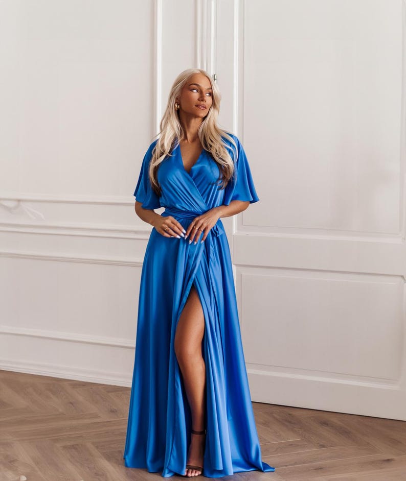 May include: A vibrant blue wrap dress with short sleeves and a high slit. The dress features a V-neckline and is made of a silky, flowing fabric. The model is wearing black sandals. The dress is suitable for formal events.