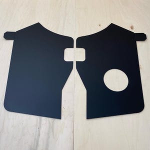 Peut inclure: Deux garde-boue en métal noir avec des découpes uniques et des pattes de fixation. L'un des garde-boue présente une ouverture circulaire. Conçus pour protéger un véhicule de la boue et des débris.