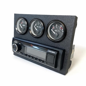 Peut inclure: Tableau de bord noir avec trois jauges et un autoradio. Les jauges affichent les lectures de volt, d'huile/kg et d'huile/°C. L'autoradio a un écran numérique et le texte "NOS128W".