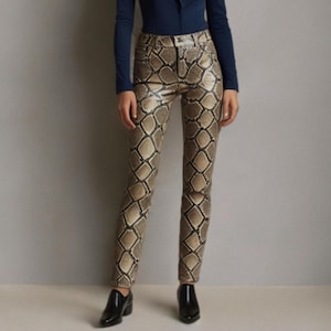 Könnte beinhalten: Eine Frau trägt ein marineblaues Oberteil mit langen Ärmeln und eine Hose mit Schlangenmuster. Die Hose hat ein sich wiederholendes Muster in neutralen Tönen. Sie trägt auch schwarze Schuhe.