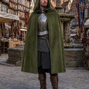 May include: A floor-length olive green hooded cloak worn over a metallic chest plate, a chainmail tunic, and a dark under-tunic. The outfit includes a brown leather belt and brown leather boots, creating a layered ensemble with a dark hood.