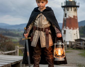 May include: A young person dressed in a medieval costume, holding a sword and a lantern. The outfit includes a black cape, tan tunic, brown pants, and boots. A lighthouse is in the background. The lantern has the text "VERITAS LUX".