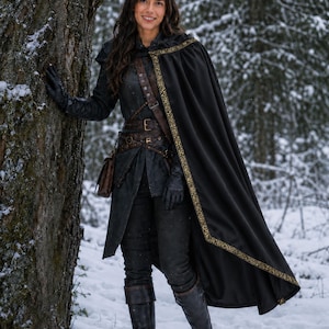 May include: A black cloak with gold trim worn over a dark textured tunic, trousers, and leather boots. The outfit includes a brown leather belt with multiple buckles and a small pouch, complemented by black leather gloves, creating a layered look.