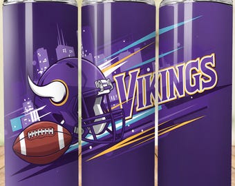 May include: A purple tumbler featuring the Minnesota Vikings logo, a football, and a helmet. The design includes the word "Vikings" in yellow and white, with a cityscape silhouette in the background. The tumbler has a straw.