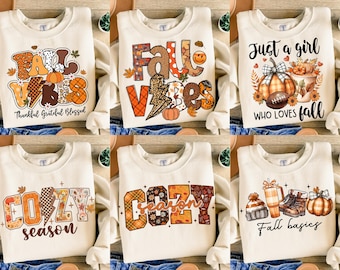 May include: Cream-colored sweatshirts with fall-themed graphics. Designs include pumpkins, leaves, and text like "Fall Vibes," "Cozy Season," and "Just a girl who loves fall." The sweatshirts are perfect for autumn.
