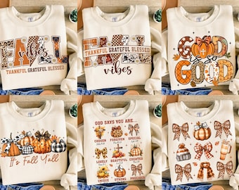 May include: Cream-colored sweatshirts with fall-themed graphics. Designs include "Fall Vibes," "Thankful Grateful Blessed Vibes," "Good is so Good," "It's Fall Y'all," and "God Says You Are..." with pumpkins, bows, and autumn leaves.