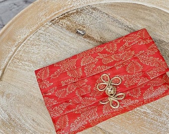Könnte beinhalten: Eine rote Stofftasche mit goldenem Blumenmuster und einem goldenen Metallverschluss.
