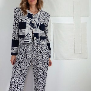 May include: A two-piece set consisting of a cropped jacket and matching trousers. The jacket features a black and white geometric pattern with solid black cuffs and a button-front closure. The trousers have a coordinating black and white print.