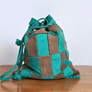 以下が含まれることがあります： 茶色とターコイズブルーのチェック柄の巾着袋。スエード製で、細長い紐と絞り口があります。