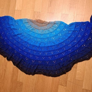 Peut inclure: Un châle fait main avec un dégradé de bleus, du clair au foncé, avec une touche de marron au centre. Le châle présente un motif ajouré et est posé sur une surface en bois. Un accessoire confortable et portable.