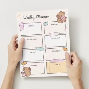 Könnte beinhalten: Ein Wochenplaner mit einem niedlichen Comic-Capybara auf dem Cover. Der Planer hat Abschnitte für jeden Tag der Woche, von Montag bis Sonntag, und einen Abschnitt für Ziele. Es gibt auch ein paar dekorative Aufkleber auf dem Planer.